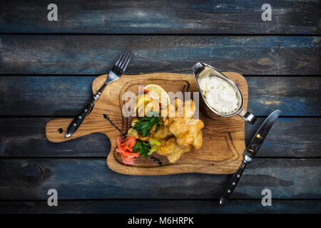 Fisch und Chips mit Sauce Tartar mit Besteck serviert. Stockfoto