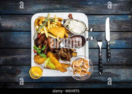 Combo snacks Komposition mit Chicken Wings, Lamm Rippen, Würstchen, gebratenen Garnelen, Zwiebelringe, nuggets Fisch und Truthähne, Tintenfischringe, suluguni mit Pommes frites und Sauce Tartar und BBQ Stockfoto