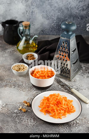 Zutaten für einen Salat aus geriebenen Karotten mit Pinienkernen auf schwarzem Hintergrund Stockfoto