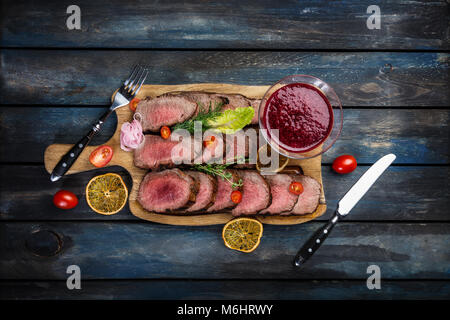 Gegrilltes Roastbeef mit Preiselbeersoße auf Schneidebrett mit Salz und Pfeffer würzen. Ansicht von oben. Stockfoto