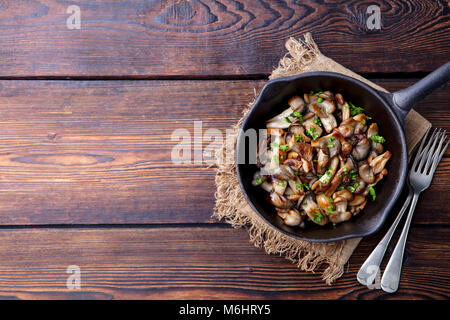 Gebratene Pilze mit frischen Kräutern in schwarzen gusseisernen Pfanne. Ansicht von oben. Kopieren Sie Platz. Stockfoto