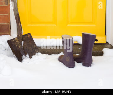 Gummistiefel und Schaufel außerhalb einer vorderen Tür in den Schnee. Stockfoto