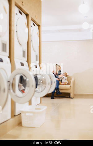 Eine Frau mit einem Kind sitzt auf dem Sofa in der Wäscherei in der Wartezeit für Kleidung Stockfoto