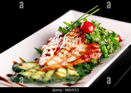 Salat serviert auf einem weißen Teller. Aal in einem Honig Sauce mit einem Salat aus einer Mischung mit Sesam bestreut, und ein paar frische Gemüse Gurke tomat Stockfoto