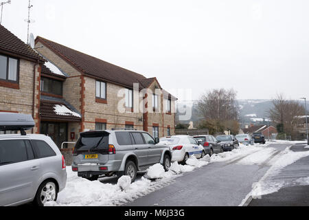 März 2018 - Die gelöschten Schnee rund um Pkw und SUV's geparkt am Straßenrand in der Somerset Village von Cheddar. Stockfoto