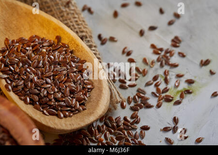 Brauner Leinsamen in Holz- Platte und Leinsamenöl in Glasflasche auf Braun rustikal Hintergrund, Ansicht von oben, Nahaufnahme, selektiven Fokus. Flachs Öl Stockfoto
