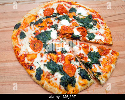 Stonebaked Pizza mit Spinat Ricotta mozarella Käse und Tomaten mit einem slice Schnitt auf einen Holzblock Stockfoto