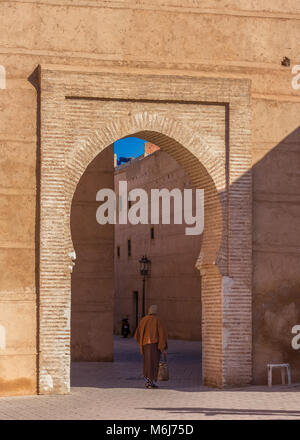 Eine lokale Frau in traditioneller Kleidung Spaziergänge durch einen alten gemauerten Torbogen in der Medina, Marrakesch, Marokko Stockfoto