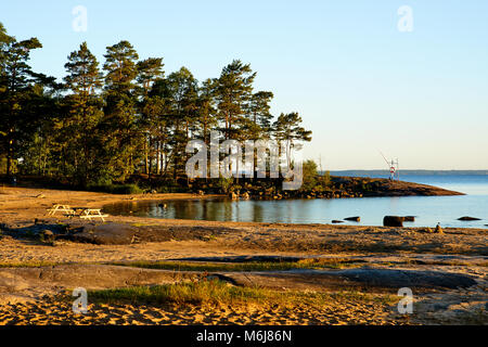Schöner Strand Landschaft mit Bäumen an der Küste des Sees Vänern in Schweden bei Sonnenaufgang. Das Wasser und der Himmel ist blau, die Sonne beleuchtet evertyhing. Stockfoto
