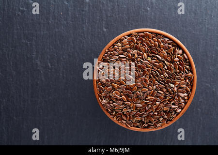 Narural raw Leinsamen in einem keramischen Ton Schüssel auf dunklem Hintergrund isoliert, close-up. Nützlich und Ernährung Ölsaaten für das tägliche Kochen. Gesunde eati Stockfoto