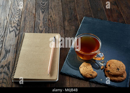 Eine innen weiß und außen braun Porzellan Tasse Kaffee mit leckeren Chocolate Chips cookies, leere Arbeitsmappe und langen gelben Bleistift mit Spitze blau auf einem dar Stockfoto