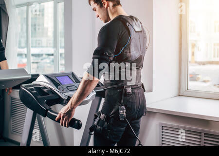 Mann im schwarzen Anzug für EMS-Training auf Laufband im Fitnessstudio Stockfoto