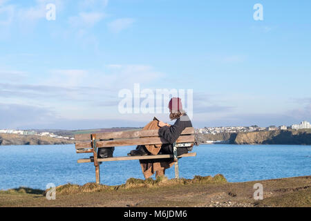 Eine Frau, die alleine auf einer Bank sitzen, ein Buch lesen zu wenig Fistral in Newquay Cornwall. Stockfoto