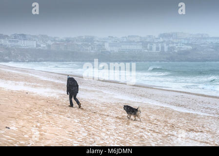 Schnee fallen, wie ein Mann mit seinem Hund über Fistral Beach in Newquay Cornwall. Stockfoto