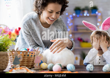 Portrait der glücklichen Mutter und kleinen Jungen tragen Häschenohren spielen mit Bunny zu Hause Ostern feiern. Stockfoto