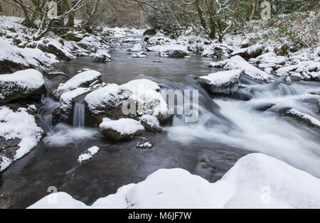 Lange Exposition von Wasser, das in einen Stream umgeben von schneebedeckten, Fluss Erme, Dartmoor, Devon. Stockfoto