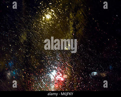 Regentropfen auf dem Fenster bei Nacht von Straßenlaternen bei starkem Regen Hintergrund beleuchtet Stockfoto