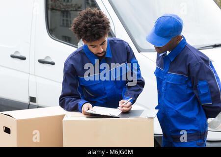 Delivery Man Schreiben auf die Zwischenablage über die Kartons durch das Fahrzeug Stockfoto