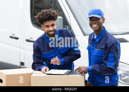 Delivery Man Schreiben auf die Zwischenablage über die Kartons durch das Fahrzeug Stockfoto