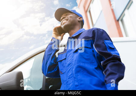 Low Angle View von Happy Lieferung junge Mann stand in der Nähe von Van Gespräch am Handy Stockfoto