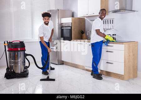 Zwei junge männliche Hausmeister in Uniform der Induktionsherd und Reinigung des Bodens in der Küche Stockfoto