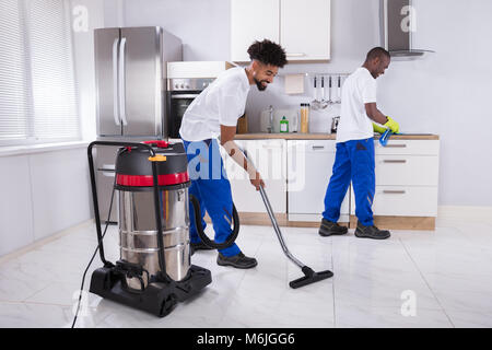 Zwei junge männliche Hausmeister in Uniform der Induktionsherd und Reinigung des Bodens in der Küche Stockfoto