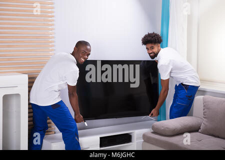 Portrait von zwei lächelnde Junge männliche Movers Platzieren den Fernseher im Wohnzimmer Stockfoto