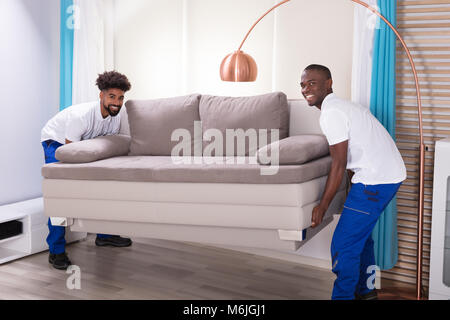 Zwei junge männliche Movers in die weiße Uniform, das Sofa im Wohnzimmer Stockfoto