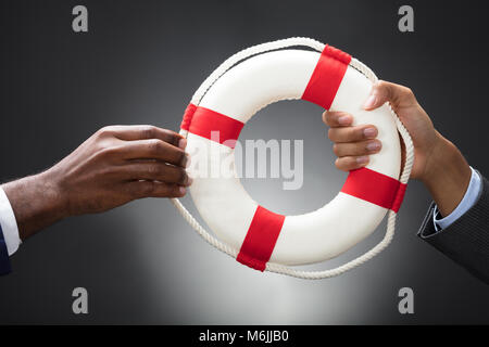 Geschäftsleute halten ein Rettungsring in den Händen auf grauem Hintergrund Stockfoto