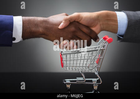 In der Nähe von zwei Geschäftsmann Hände schütteln Vor leeren Warenkorb auf grauem Hintergrund Stockfoto