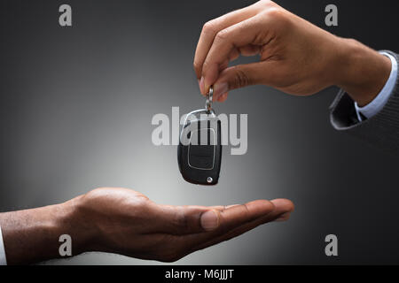 Nahaufnahme der Hand Übergabe Auto Schlüssel zu der Person, gegen grauer Hintergrund Stockfoto