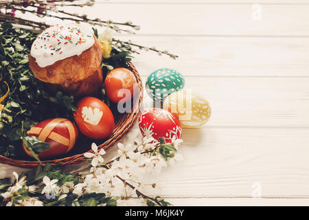 Stilvolle Ostereiern und Ostern Brot Kuchen und Blumen auf Holzuntergrund. Moderne Eier natürlich gefärbt. willow Knospen und Weidenkorb. Platz für Text. h Stockfoto