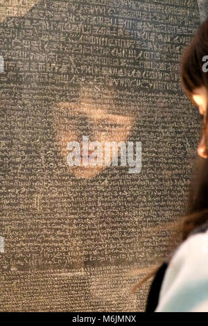 Mädchen Gesicht spiegelte, als sie versucht, den Stein von Rosette mit Schreiben in verschiedenen alten Sprachen-selektiven Fokus - im British Museum London U zu lesen Stockfoto