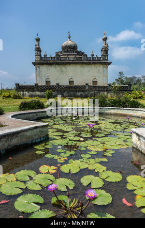 Madikeri, Indien - 31. Oktober 2013: Royal weiß und grau Mausoleum hinter Teich mit Seerosen im grünen Garten der Domäne Raja Gräber unter Set blau s Stockfoto