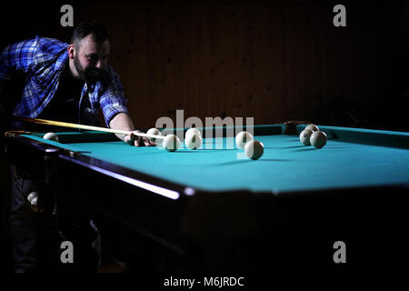 Ein Mann mit einem Bart spielt eine große Billard. Partei in einem 12-Fuß-Pool Stockfoto