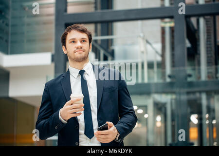 Sicher Mann mit Kaffeetasse und über sein Smartphone während des Gehens in Halle Stockfoto