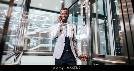 Afroamerican Geschäftsmann in der modernen Aufzug aus Glas am Telefon sprechen Stockfoto