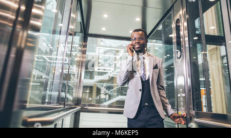 Afroamerican Geschäftsmann in der modernen Aufzug aus Glas am Telefon sprechen Stockfoto