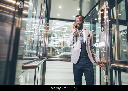 Afroamerican Geschäftsmann in der modernen Aufzug aus Glas am Telefon sprechen Stockfoto