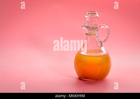 Ungefilterte, roh Apfelessig mit Mutter - ein Glas cruet gegen rosa Hintergrund Stockfoto