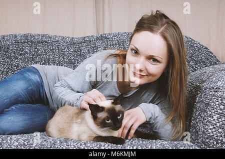 Glückliche junge Frau entspannt auf einem Sofa mit cat Stockfoto
