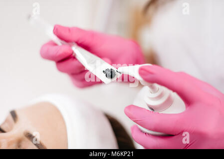 Hautpflege und Kosmetik Konzept. Die kosmetikerin ist die spezielle schwarze Creme aus der Flasche auf die Bürste. Immer bereit zu Laser und Ultraschall Gesichtsbehandlung. Stockfoto