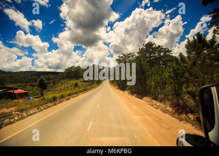 Sonnigen highway verschwindet in den Raum zwischen den hügeligen Land Land gegen bewölkt blauer Himmel Stockfoto