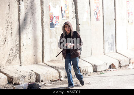 Kalandia, Palästina, 12. Januar 2011: Ein Junge wird durch eine Betonwand in der Nähe von Kalandia Check Point von Israel gebaut Palästinenser pendeln in Ea zu stoppen Stockfoto