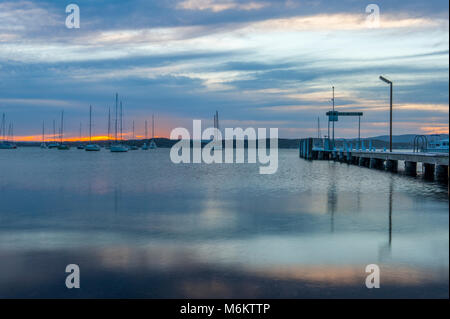 Sonnenuntergang am Lake Macquarie mit Belmont Wharf im Vordergrund und Segelboote im Hintergrund. Belmont. Australien Stockfoto