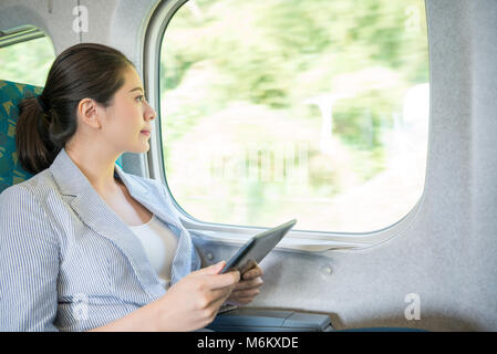 Charmante asiatische Mädchen immer noch die Arbeit mit Ihren digitalen tablet Suche im Internet durch eine Verbindung zum WLAN des Zuges auf der Reise. Stockfoto