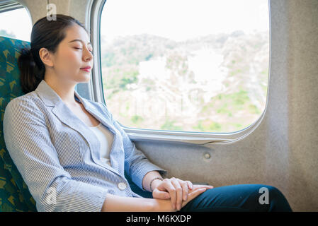 Hart arbeiten, schöne asiatische Business woman einen erholsamen Schlaf auf den fahrenden Zug für Ihre künftige Reise nehmen. Stockfoto