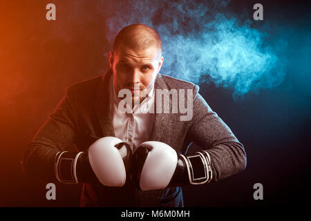 Junge intelligenter Mann Geschäftsmann in weißem Hemd, Grau, Schwarz und Weiß Boxhandschuhe in vor dem Hintergrund der roten und blauen Rauch posing von einem Stockfoto
