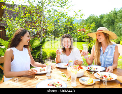 Gerne weibliche Freunde mit Gläser limonade am Esstisch in Rasen Stockfoto