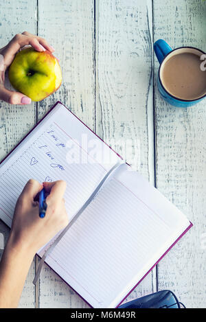 Notebook, Apple und Kaffee mit Milch und Sonnenblumenkerne auf dem Tisch Stockfoto